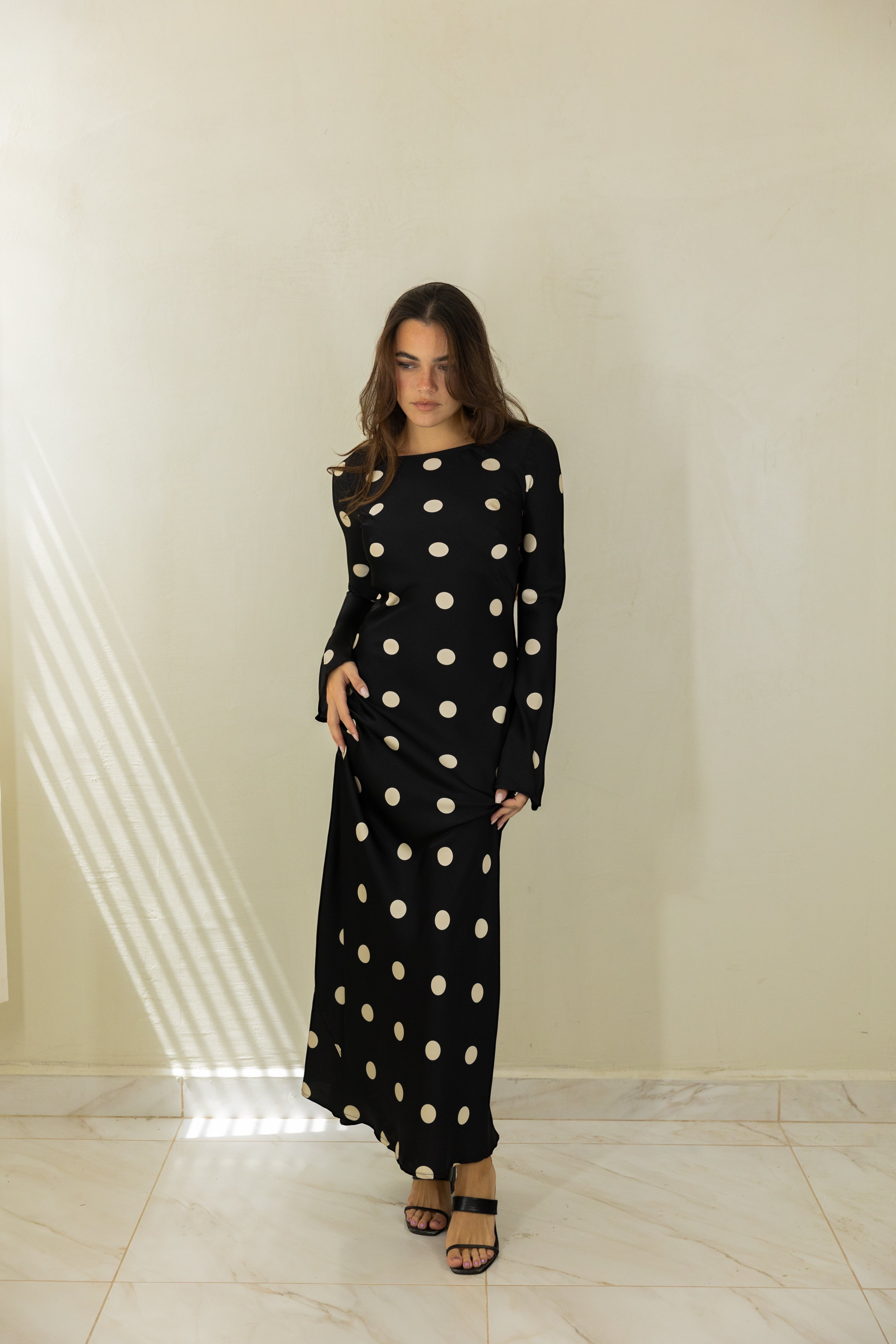 Model wearing an ISSUE 92 black maxi dress with large cream polka dots and long sleeves in a minimalist studio setting