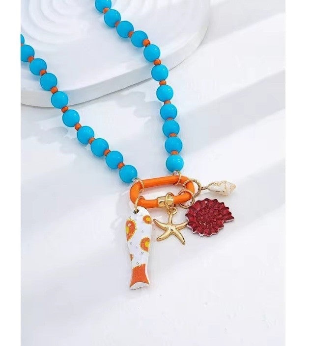 ISSUE 92 blue beaded necklace with orange accents and ocean-themed charms: fish, starfish, shell, and red coral.